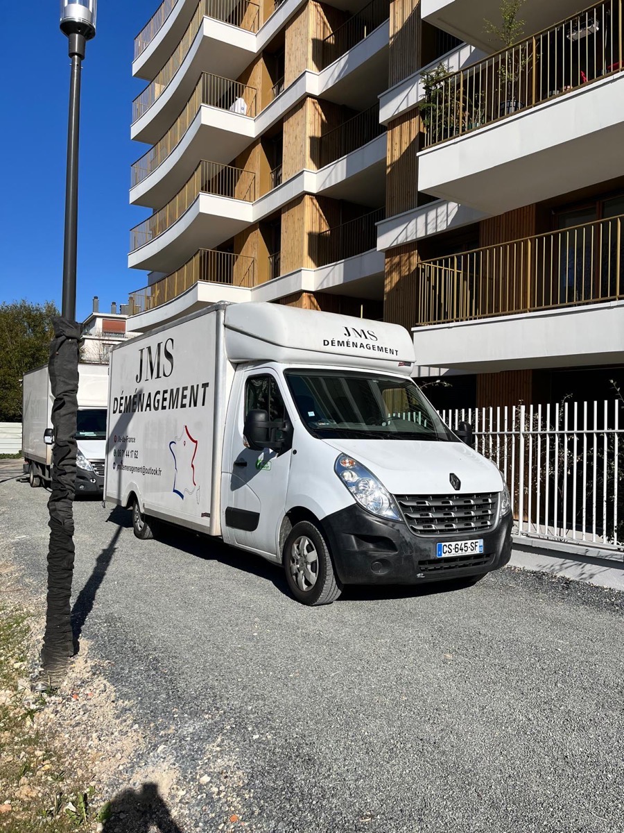 Camion JMS Déménagement brande devant une copropriete moderne